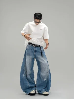 Front studio view of blue distressed ultra-wide denim jeans with oversized curved legs and five-pocket construction