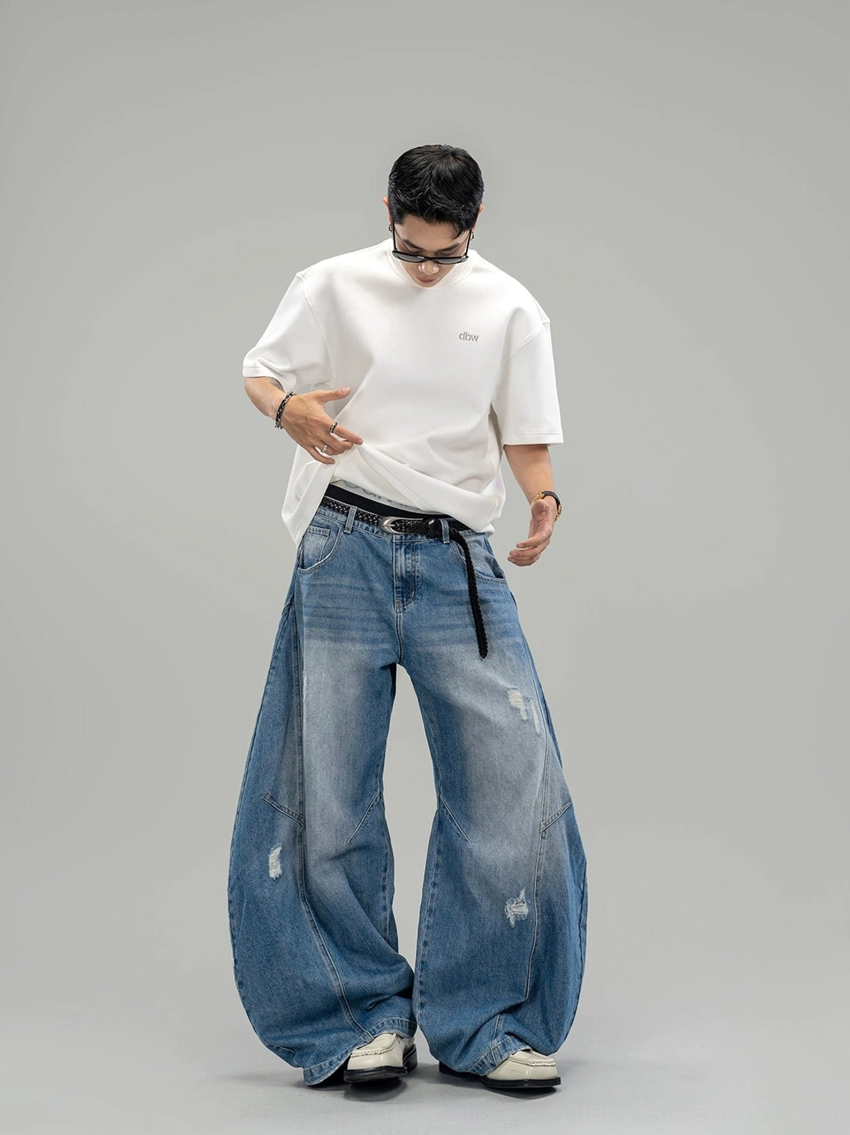 Front studio view of blue distressed ultra-wide denim jeans with oversized curved legs and five-pocket construction