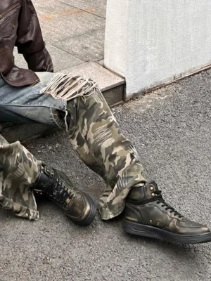 Distressed leather combat boots worn with a streetwear outfit on asphalt pavement showing the rugged black mid-top silhouette