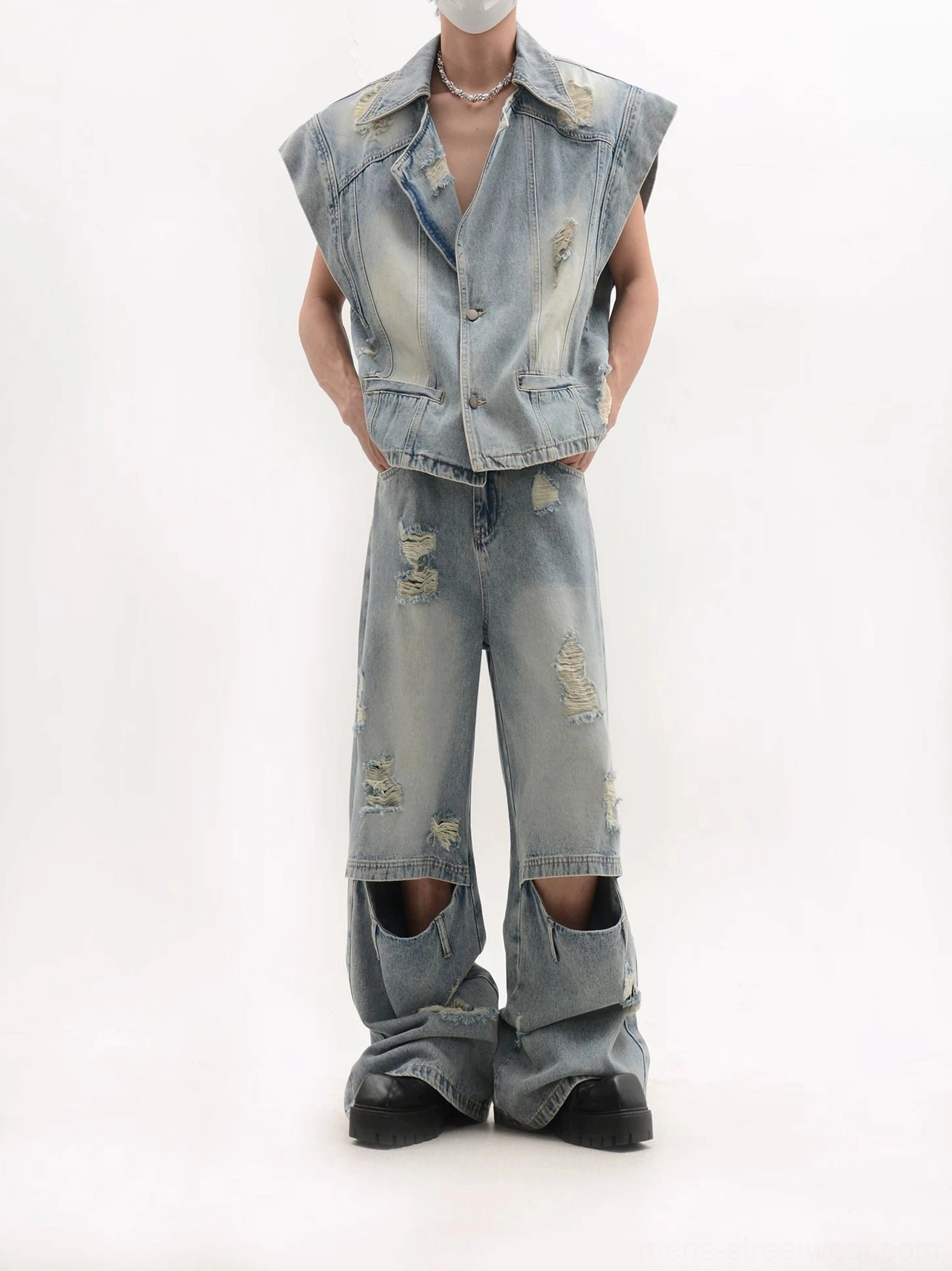 Front view of an oversized distressed blue denim vest and wide-leg jeans set styled with a pearl necklace in a minimalist studio
