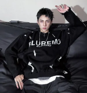 Front view of a black distressed oversized shred-knit sweater with bold chest lettering, frayed cutouts, dropped shoulders, and layered white hem styled with black cargo pants