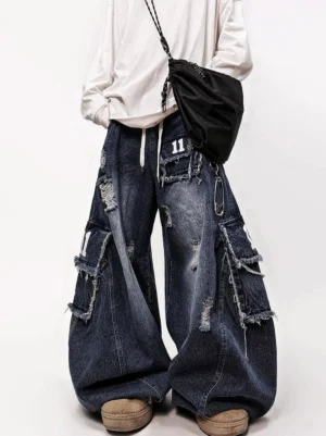 Low front view of distressed patch cargo wide-leg jeans in dark indigo washed denim with oversized legs, frayed tears, utility pockets, and number 11 badge