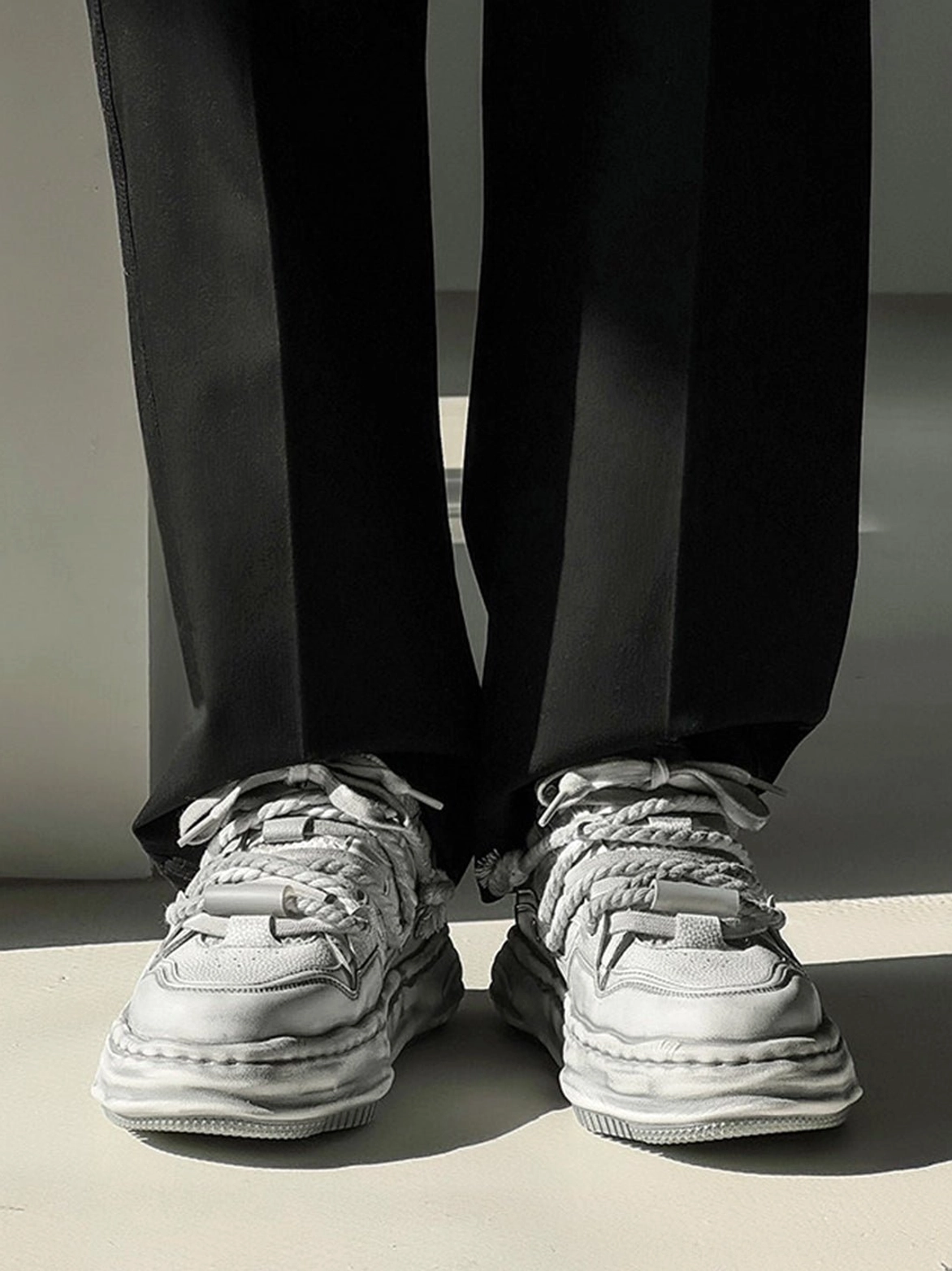 Front view of distressed platform sneakers worn with straight black trousers showing the layered upper and thick sculpted sole