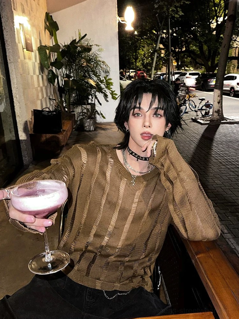 Front three-quarter view of an oversized distressed vertical stripe sheer knit sweater in earthy yellow brown worn with punk-inspired streetwear at a night cafe