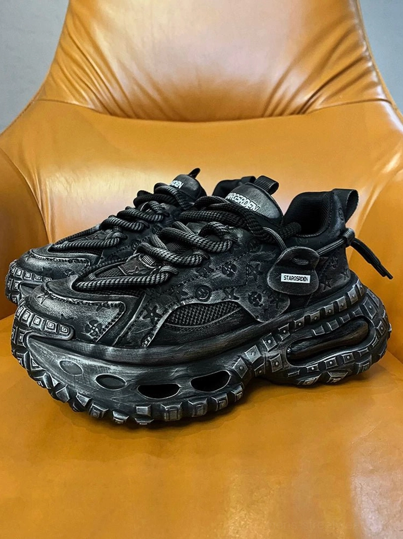 Black distressed chunky platform sneaker in a front three-quarter view showing the hollow sculpted sole, embossed upper, thick rope laces, and dark techwear styling