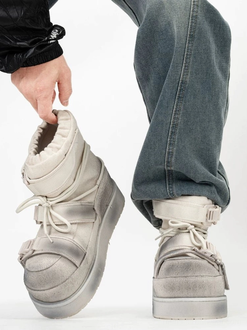 Distressed white quilted platform moon boots with buckle straps and lace-up closure worn with blue jeans in side view