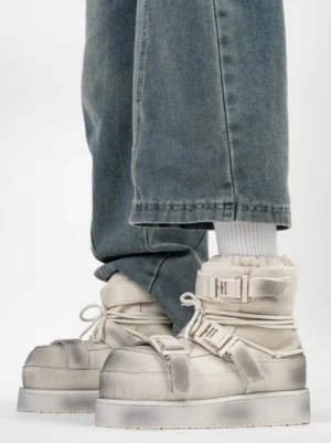 Distressed white triple-buckle platform winter boots worn with loose blue jeans, featuring fleece collar and lace-up front