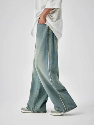 Left side view of distressed vintage blue wide-leg denim jeans with contrast stitching and frayed hem styled with an oversized gray streetwear T-shirt and sneakers