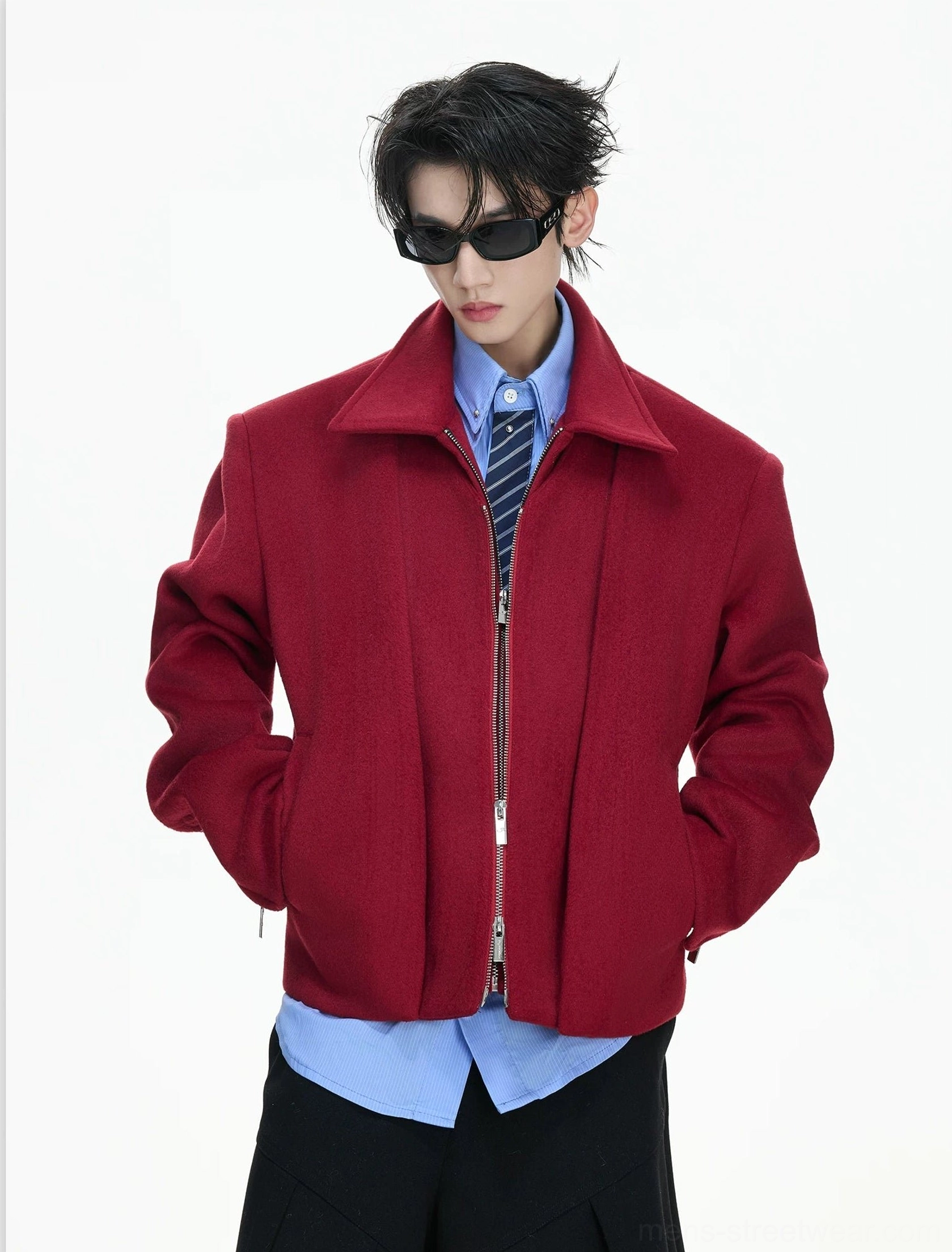Front full-body view of a structured double-zip sculpted cropped wool jacket styled with a blue shirt striped tie and black sunglasses