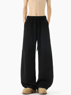 Black oversized wide-leg sweatpants shown in a full front view with elastic drawstring waistband, soft fleece-like texture, relaxed Korean streetwear fit, and casual leather sneakers