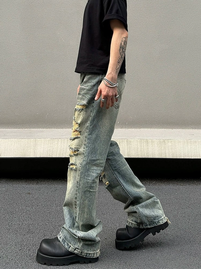 Side rear view of shredded blue denim flared jeans featuring frayed raw hems and distressed lower legs