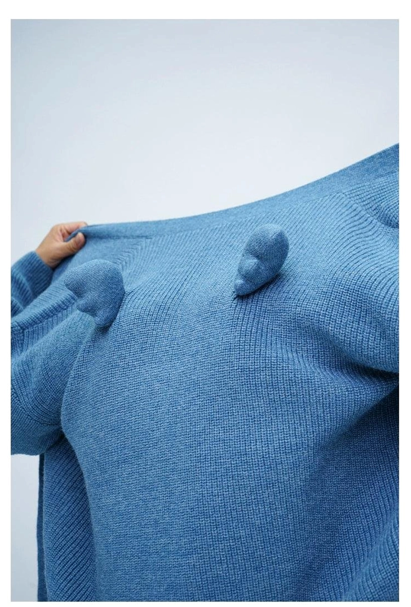 Close-up of dusty blue fuzzy ribbed knit cardigan fabric with decorative wing-shaped pom-poms on the back