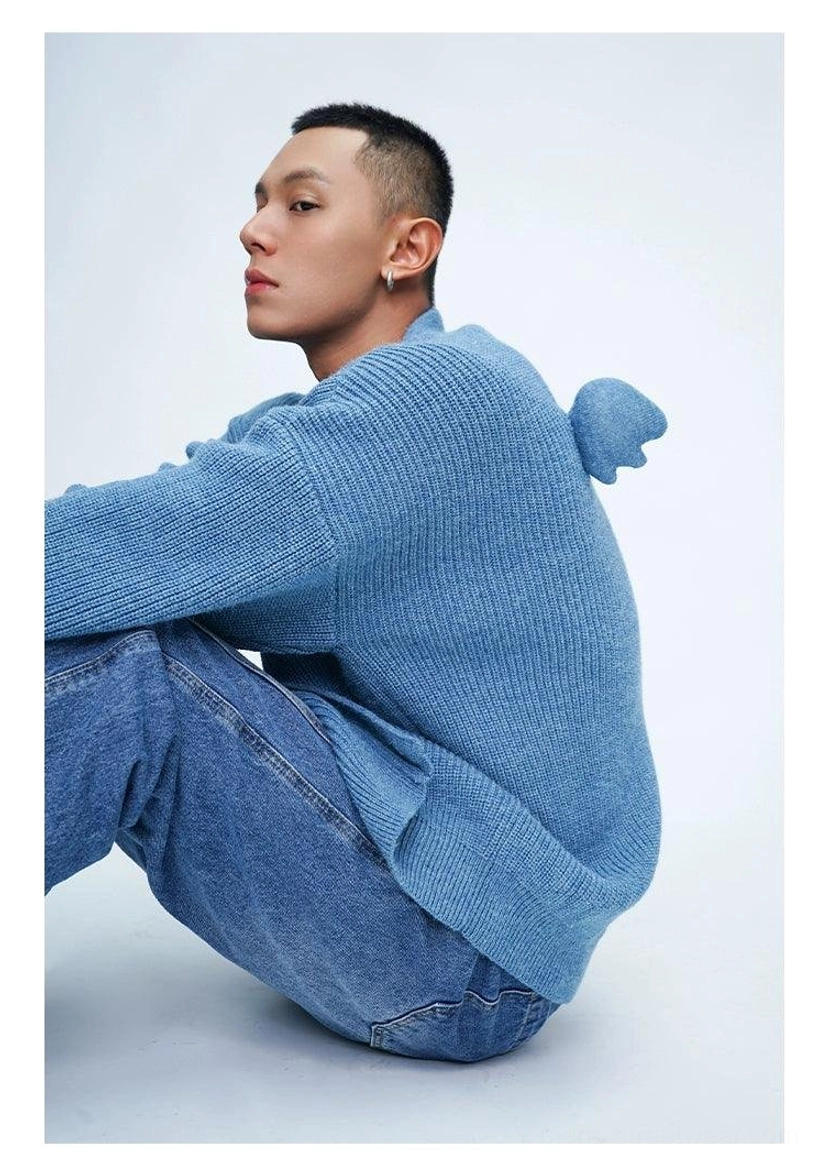 Male model wearing a dusty blue oversized fuzzy knit cardigan with wing pom-pom back decoration and relaxed denim streetwear styling