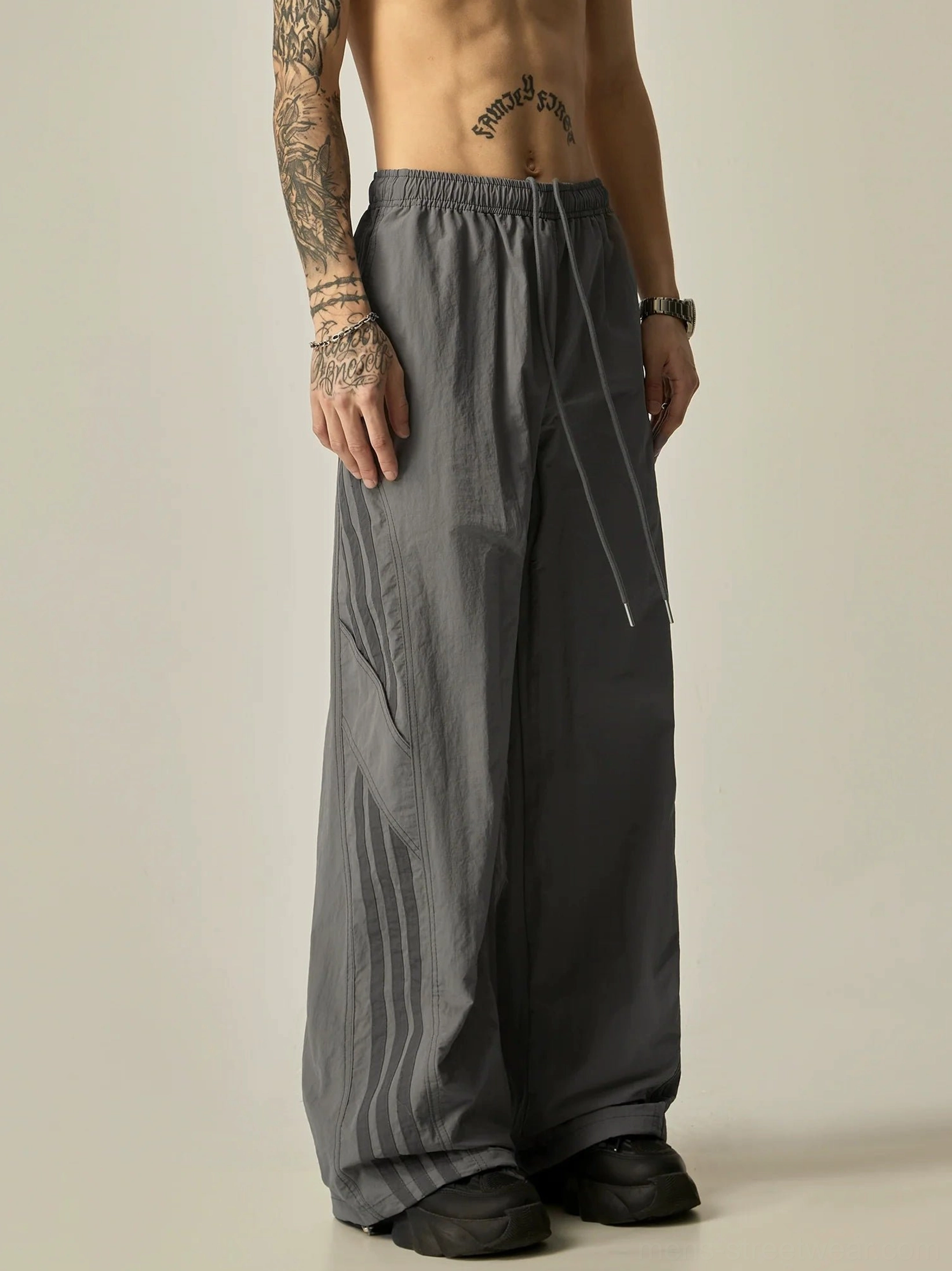 Side view of dusty gray wide-leg track pants with subtle dark gray side stripe detail, drawstring waist, and loose full-length fit