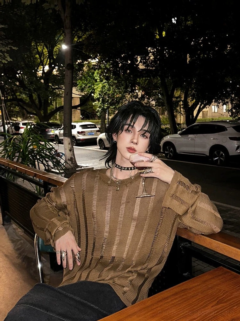 Side seated styling view of an earthy yellow brown distressed vertical ladder knit sweater with long loose sleeves and transparent stripe texture