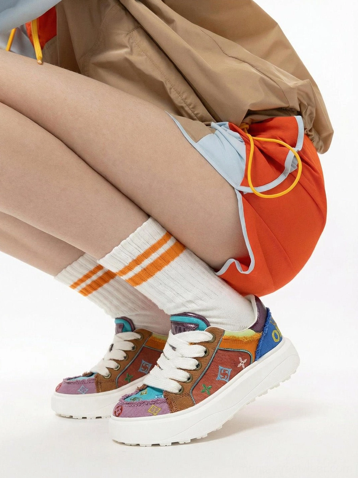 Overhead view of multicolor embroidered platform skate sneakers worn with orange sport shorts and striped socks showing the chunky outsole and side profile