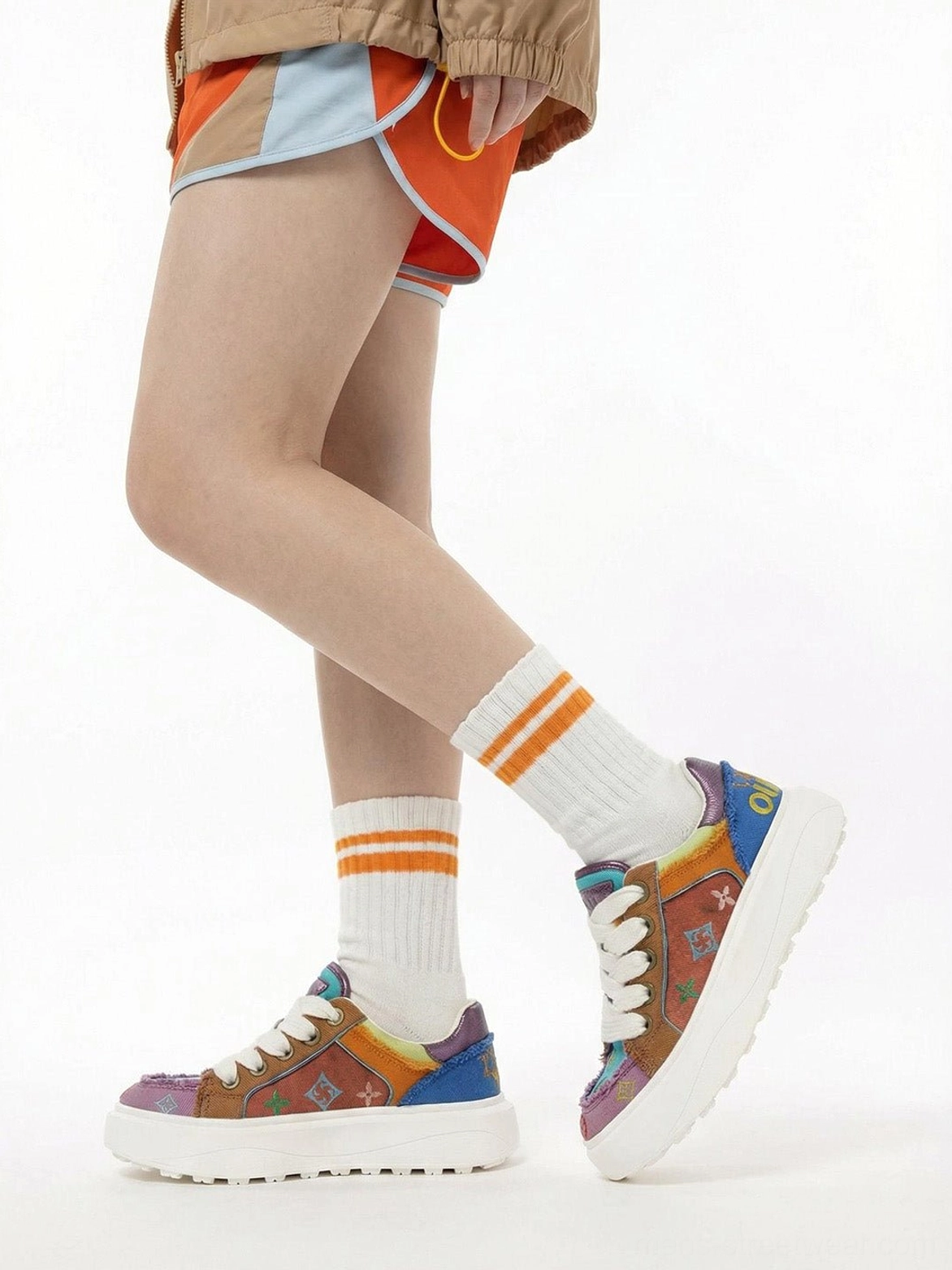 Model wearing multicolor platform skate sneakers with orange contrast shorts cropped streetwear jacket and striped crew socks in a low angle Seoul street style outfit