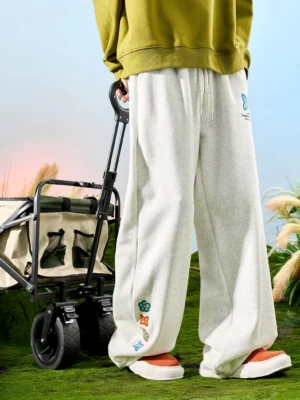 Heather light grey embroidered floral wide-leg sweatpants styled with an olive sweatshirt in an outdoor grassy setting