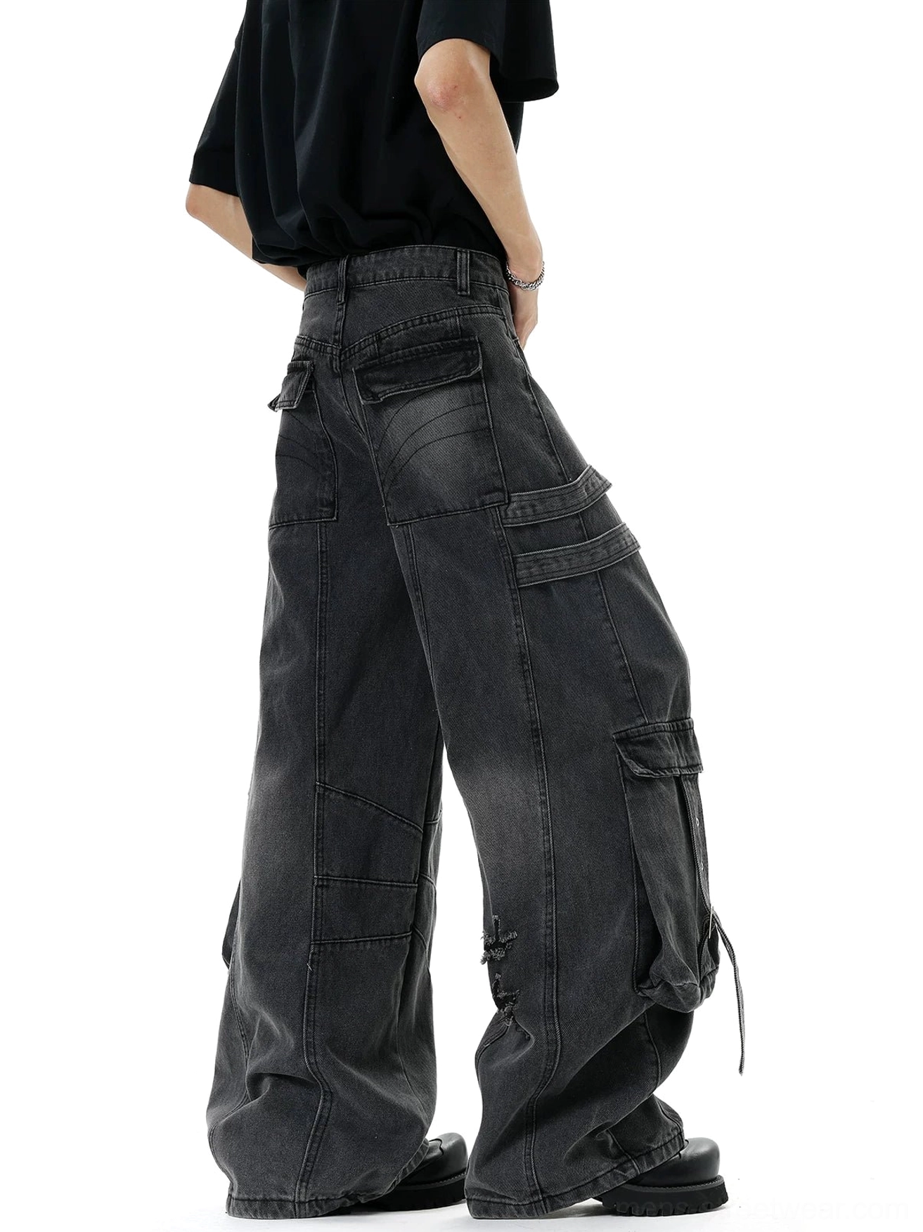 Side rear view of faded black wide-leg cargo denim jeans with relaxed fit, utility side pockets, and deconstructed streetwear details