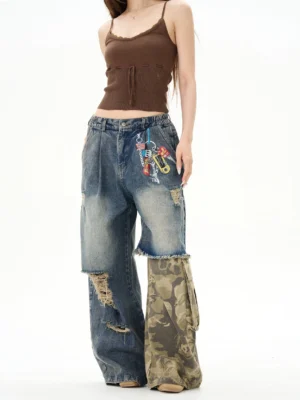 Front view of faded blue distressed patchwork wide-leg denim jeans on a female model with camo lower-leg panels and decorative keychains