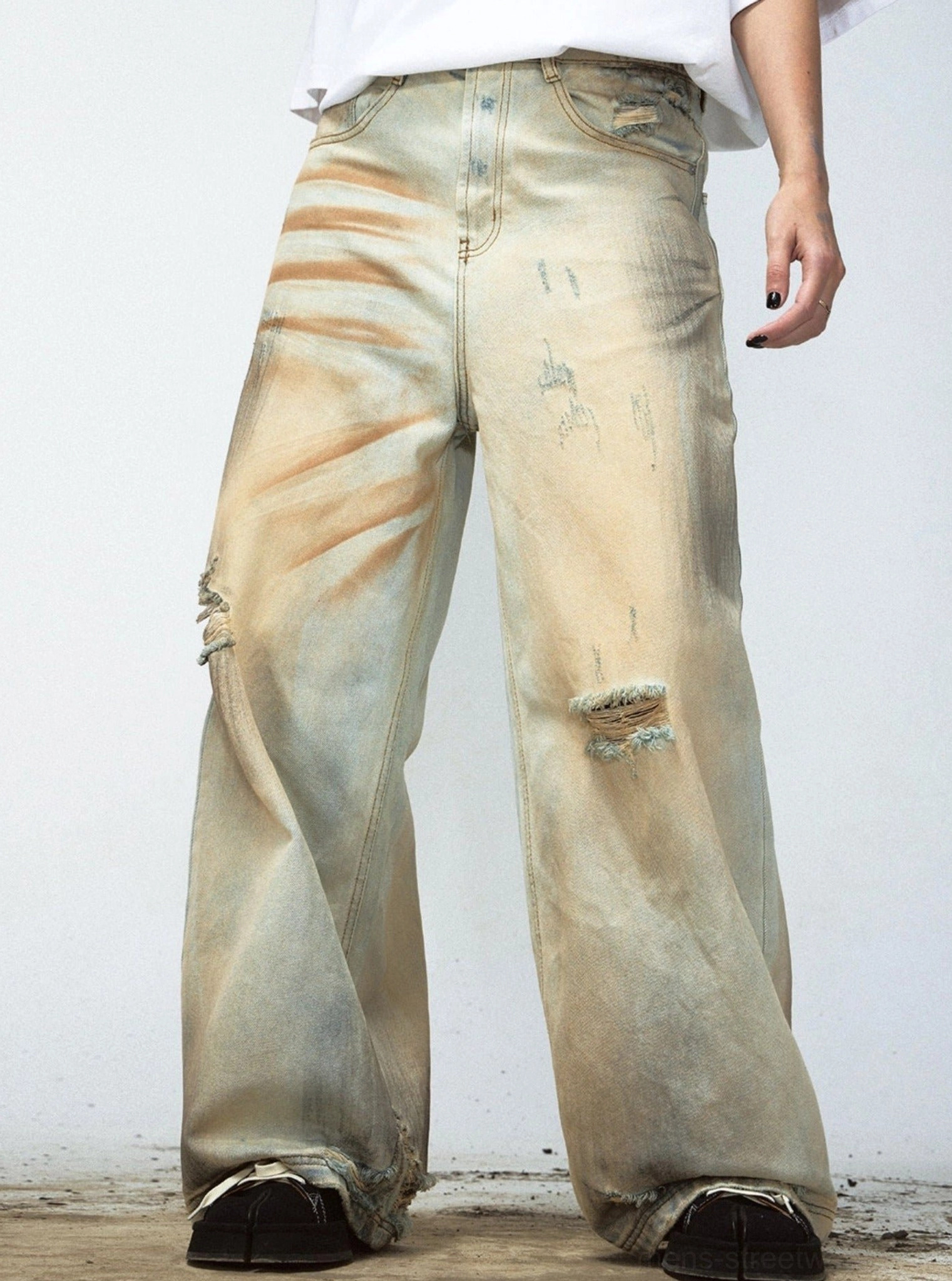 Side close view of faded yellow retro denim pants showing raw hem and ripped knee streetwear details