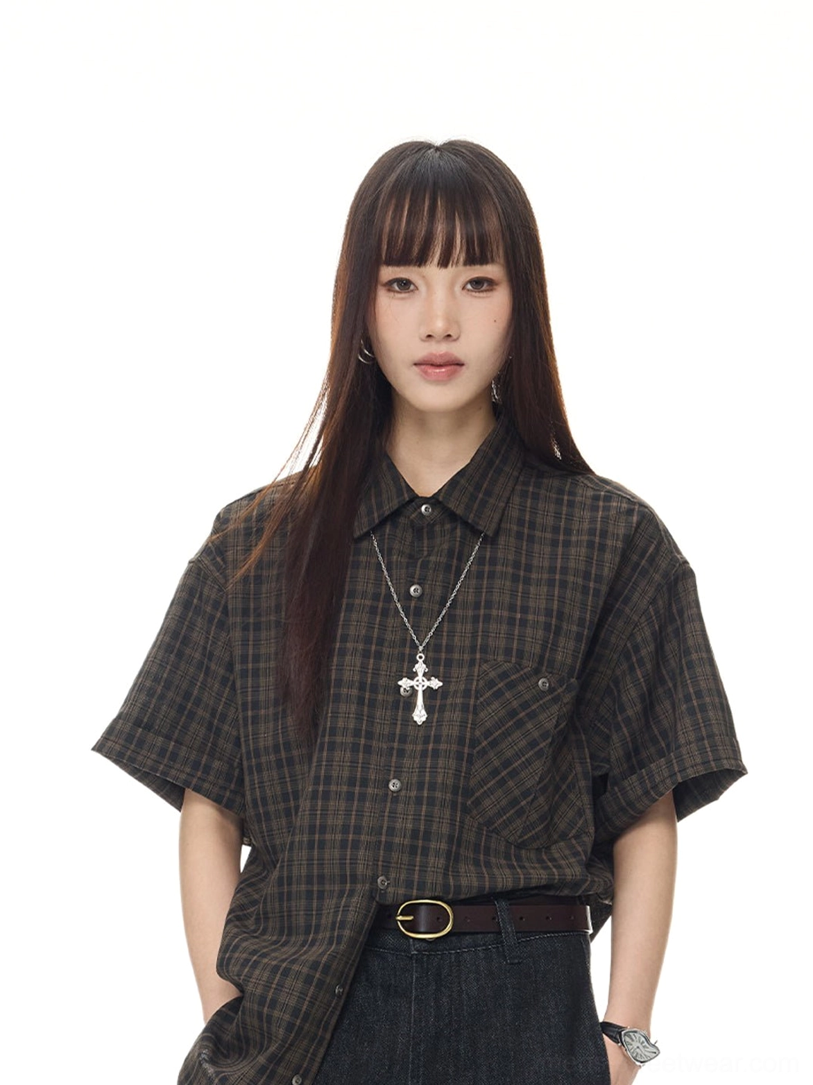 Female model in a relaxed dark brown plaid short sleeve streetwear shirt styled with a leather belt and cross necklace
