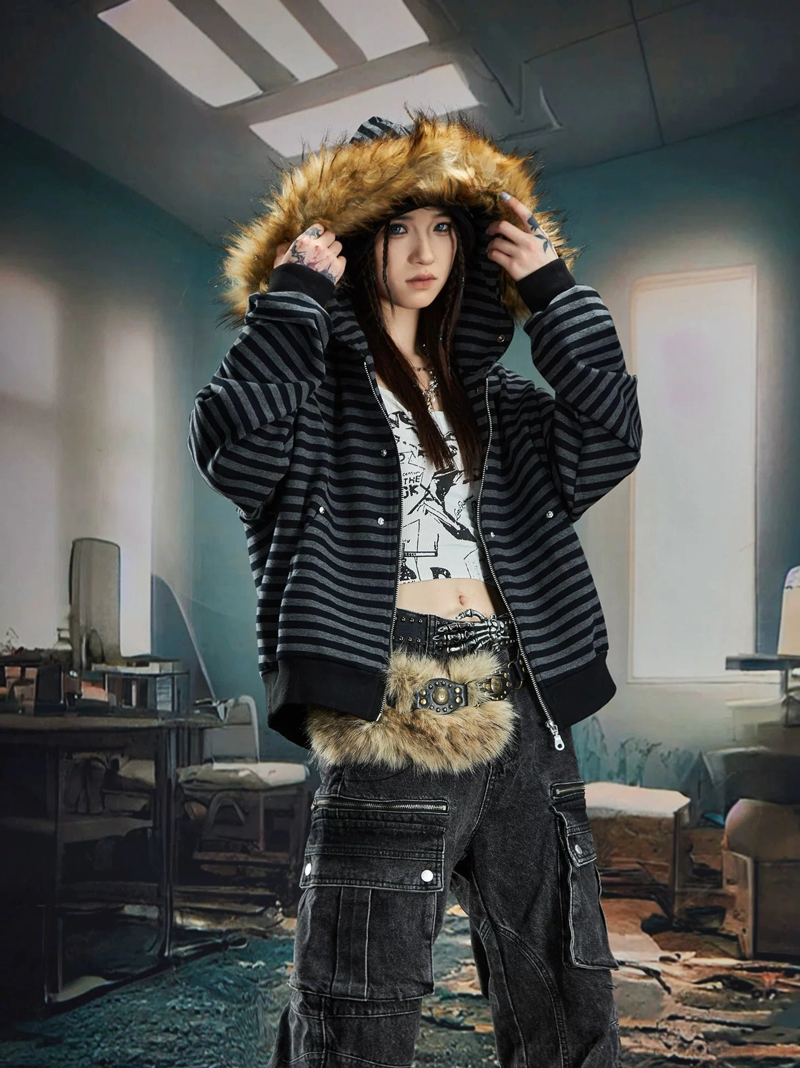 Black and grey striped faux fur trim hooded zip-up streetwear jacket worn by female model with cargo jeans in industrial setting