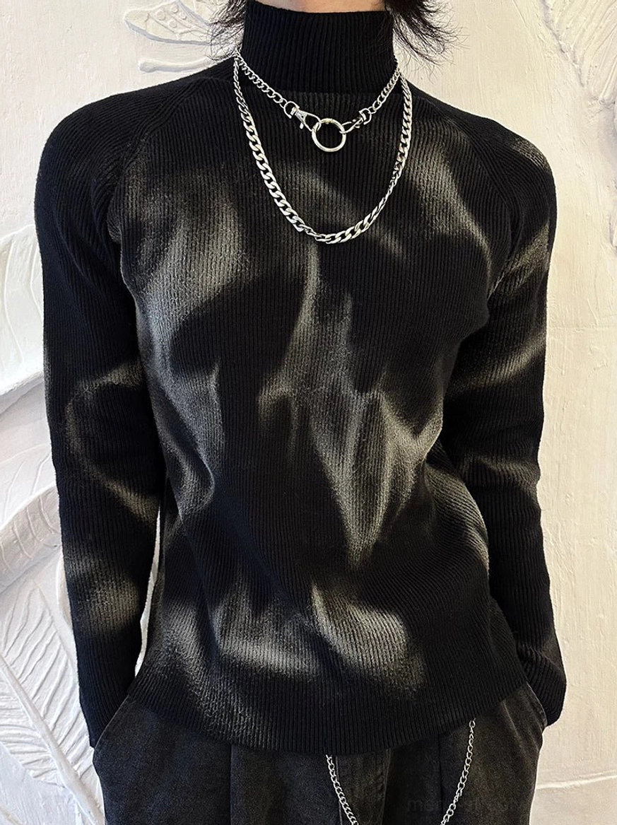 Front upper-body view of fitted black ribbed turtleneck sweater featuring irregular grey spray highlights and textured knit fabric