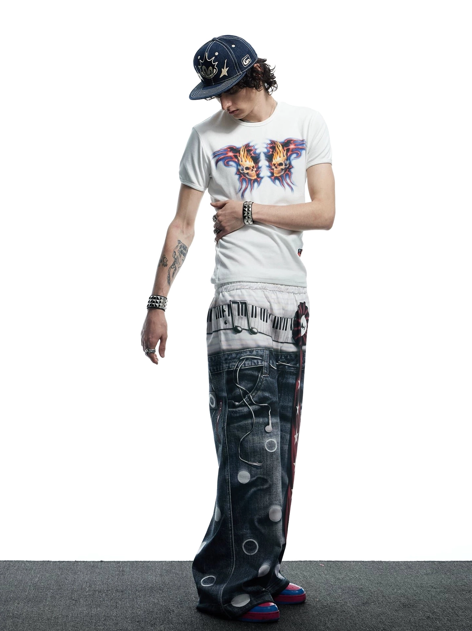 Back three-quarter view of white flaming skull graphic baby tee styled with a printed baseball cap and monogram wide-leg jeans