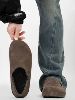 Dark brown fleece-lined suede leather clogs worn with blue jeans, overhead close-up showing plush interior lining and metal side button