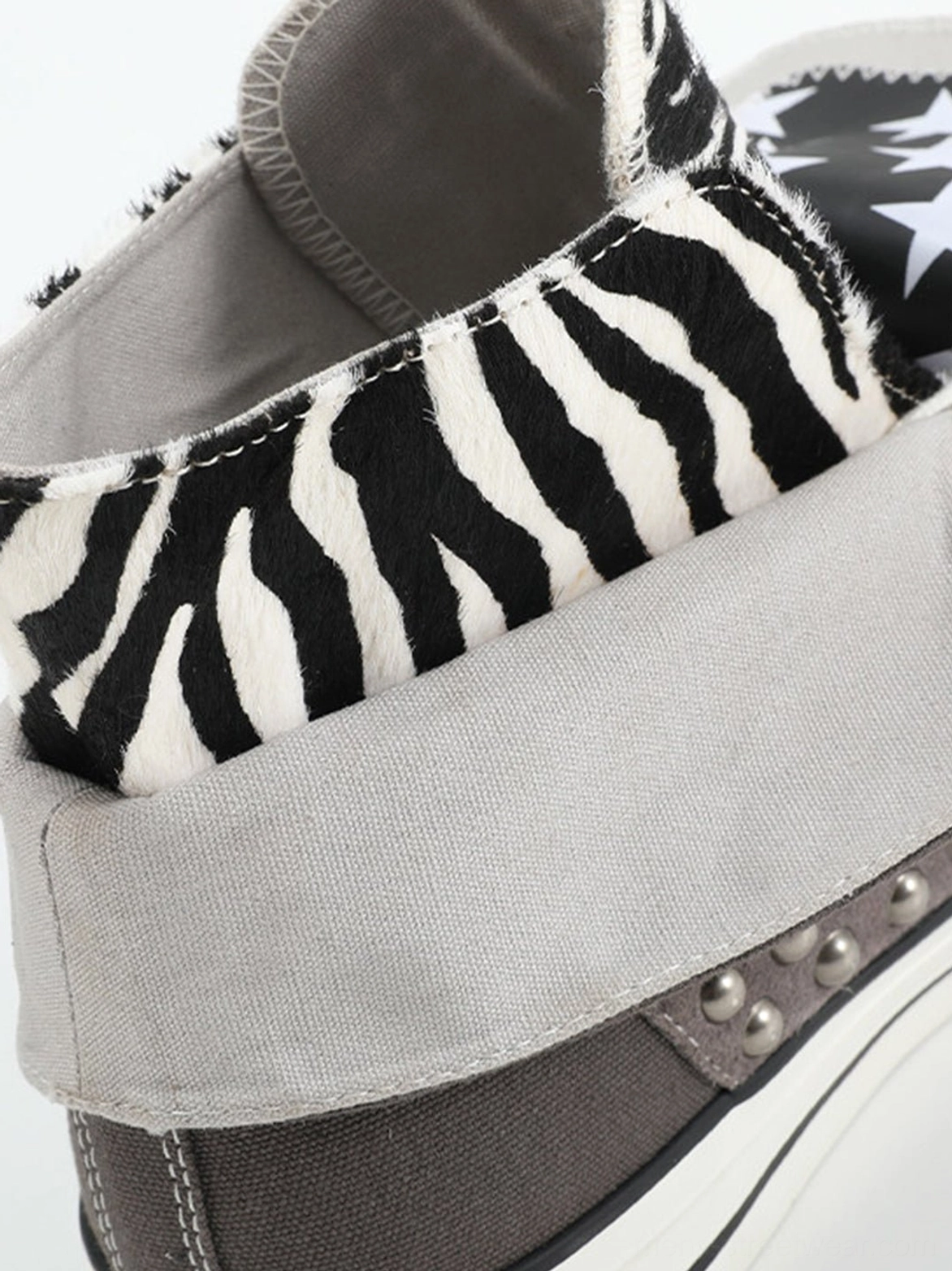 Close-up of foldable fuzzy zebra print sneaker collar with gray canvas binding trim and small silver studs