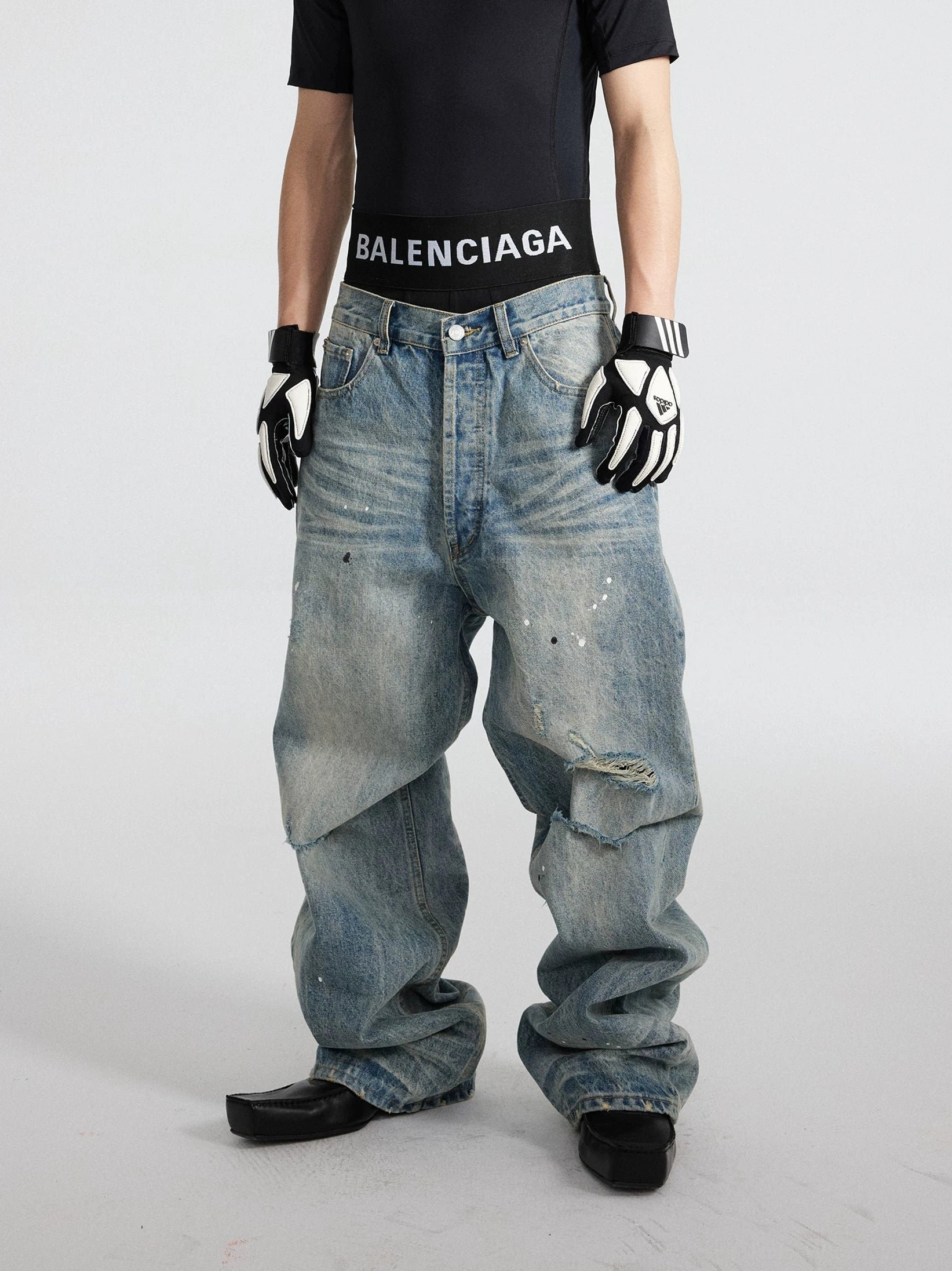 Full front view of distressed blue paint splatter streetwear jeans with ripped knee, acid wash finish, and oversized wide legs