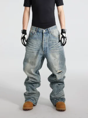Front view of distressed blue paint splatter wide-leg jeans with ripped knee, faded whiskering, and baggy stacked denim silhouette