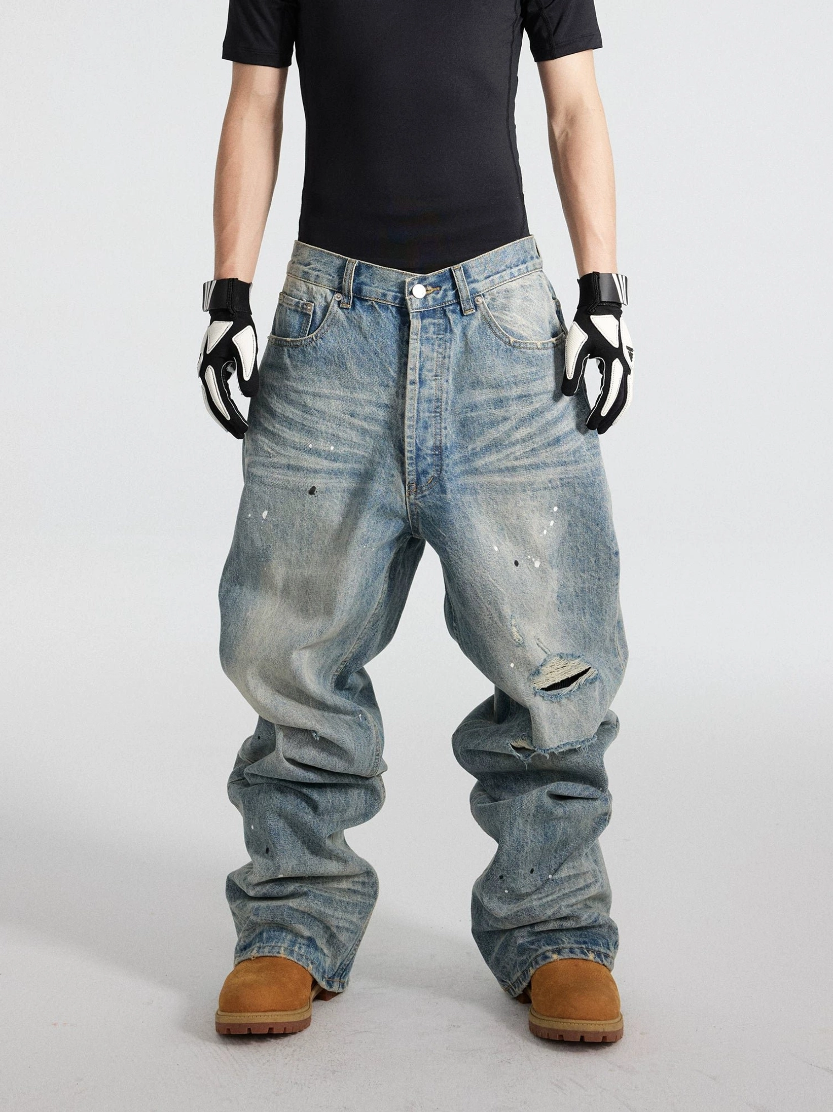 Front view of distressed blue paint splatter wide-leg jeans with ripped knee, faded whiskering, and baggy stacked denim silhouette