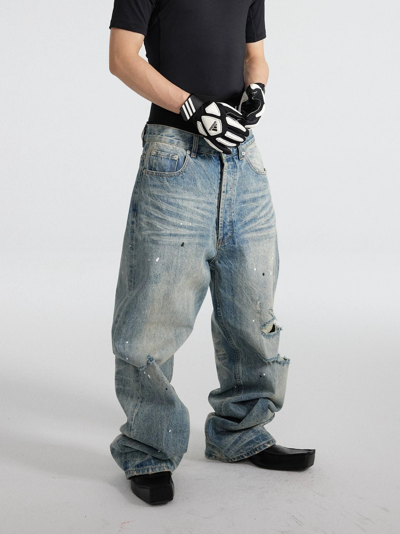 Three-quarter front view of light blue distressed wide-leg jeans featuring paint splatter details, ripped knee, and loose stacked silhouette