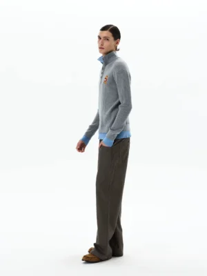 Side view of men's grey ribbed knit polo sweater featuring sky blue layered collar cuffs and hem with brown trousers and loafers