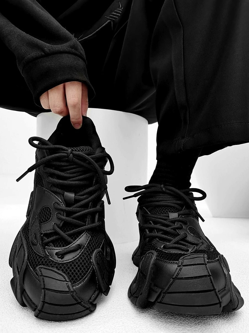 Black futuristic chunky platform sneakers held with black streetwear outfit, breathable mesh upper, lace-up closure, and rugged techwear rubber outsole