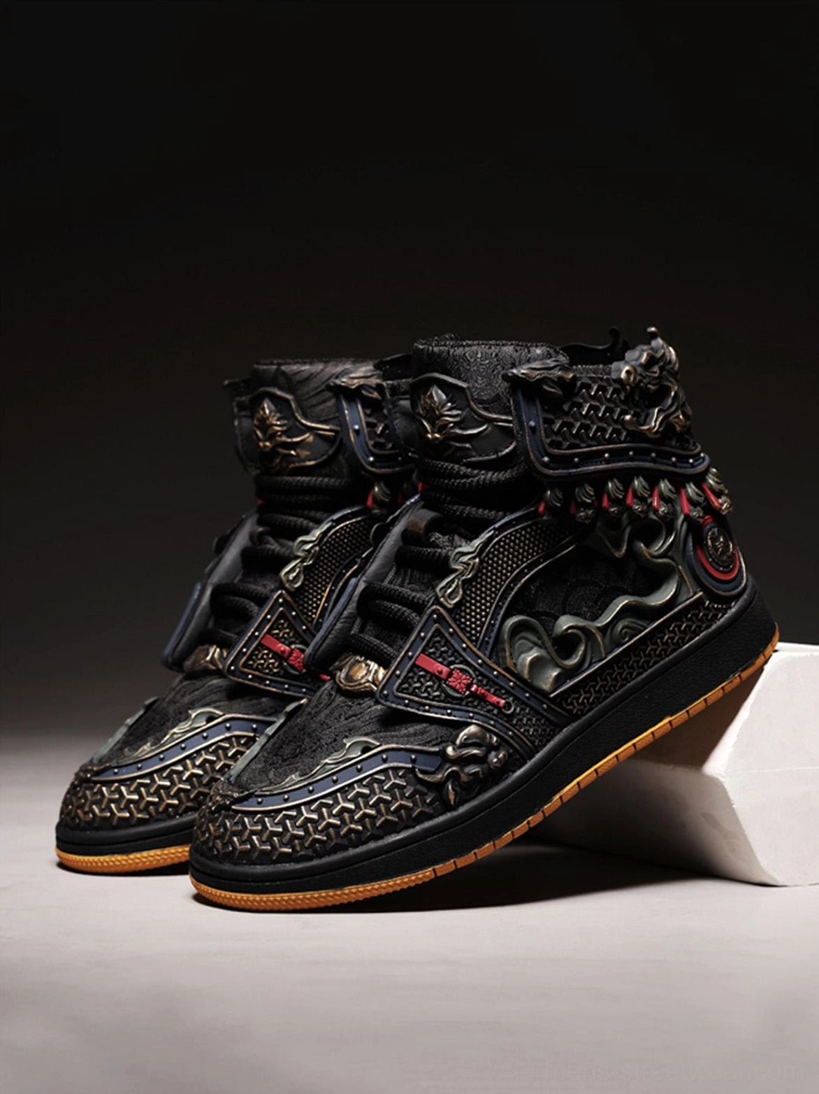 Oblique front view of black mythic armor high-top sneakers showing the toe cap, ornamental side patterns, and gum rubber outsole