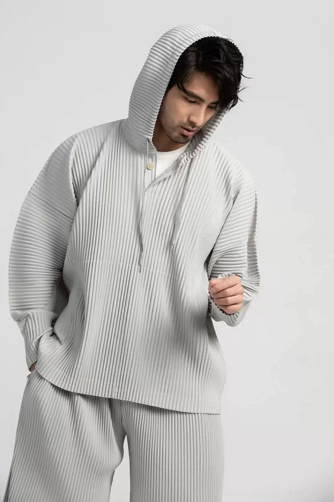 Grey Glacier Wave pleated hoodie and pants outfit shown from a low three-quarter front angle with textured fabric and relaxed silhouette