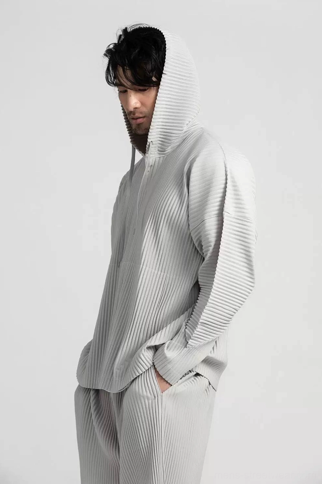 Side profile of a man wearing the Glacier Wave grey pleated hoodie set with the hood up and loose vertical pleated texture