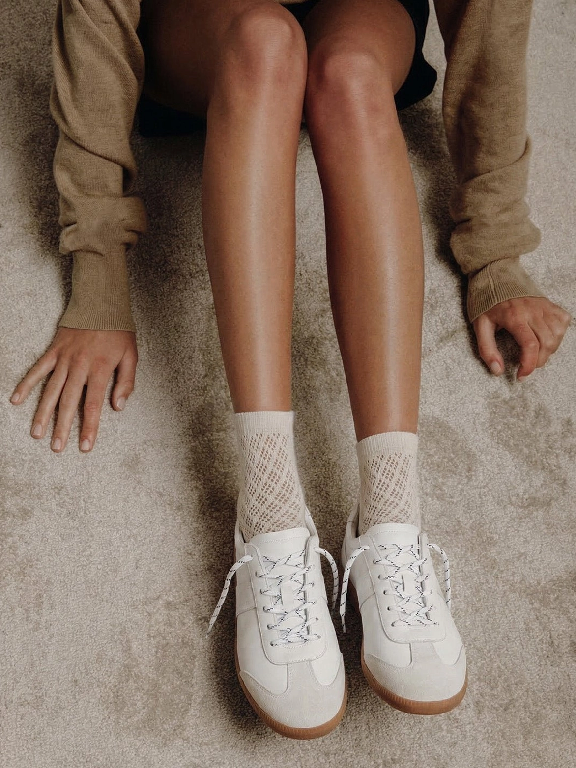 Pair of off-white gloss-finish suede leather low-profile trainers styled with beige socks in an overhead lifestyle view