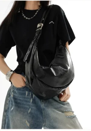Glossy black buckle crescent sling bag worn with cropped black tee and ripped denim for Y2K streetwear styling