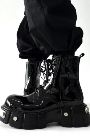 Side view of glossy black patent leather platform combat boots worn with cropped black cargo pants, showing side zipper and metal-trimmed lug sole