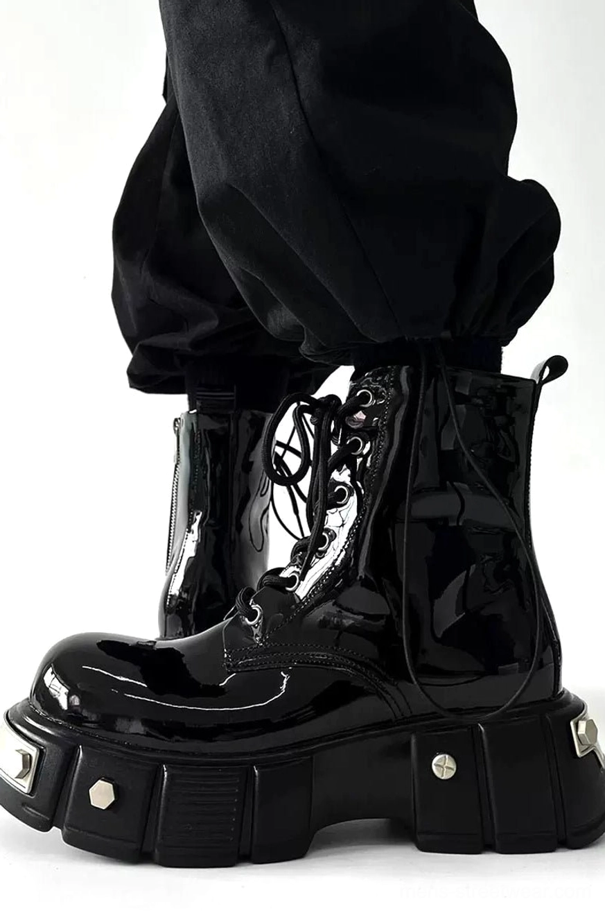 Side view of glossy black patent leather platform combat boots worn with cropped black cargo pants, showing side zipper and metal-trimmed lug sole