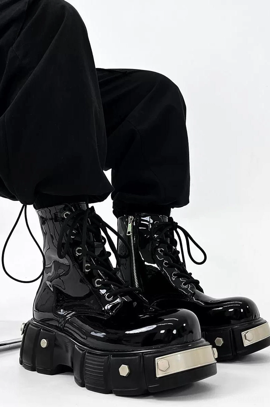 Overhead view of glossy black lace-up patent leather platform combat boots worn with cropped black cargo pants, showing silver metal sole accents