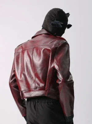 Glossy crimson burgundy faux leather moto jacket rear three quarter view showing tailored back seams adjustable waist strap and fitted sleeves
