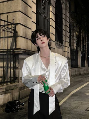 White glossy satin tie-neck shirt with loose button-front fit and long matching neck tie on an old European street