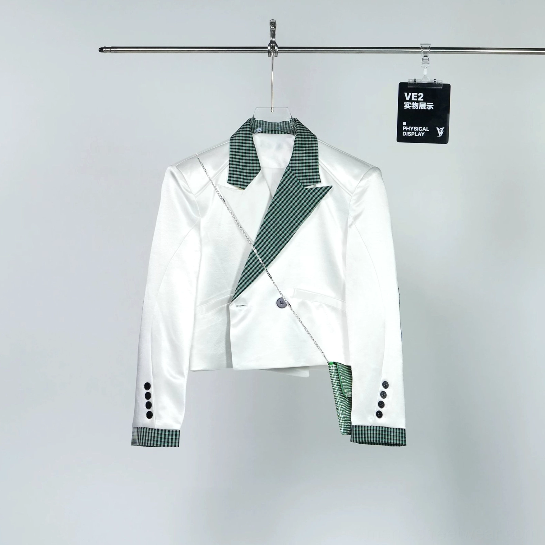 Hanging front view of the glossy white cropped tuxedo blazer with green check lapel and cuff trim and attached chain-strap accent