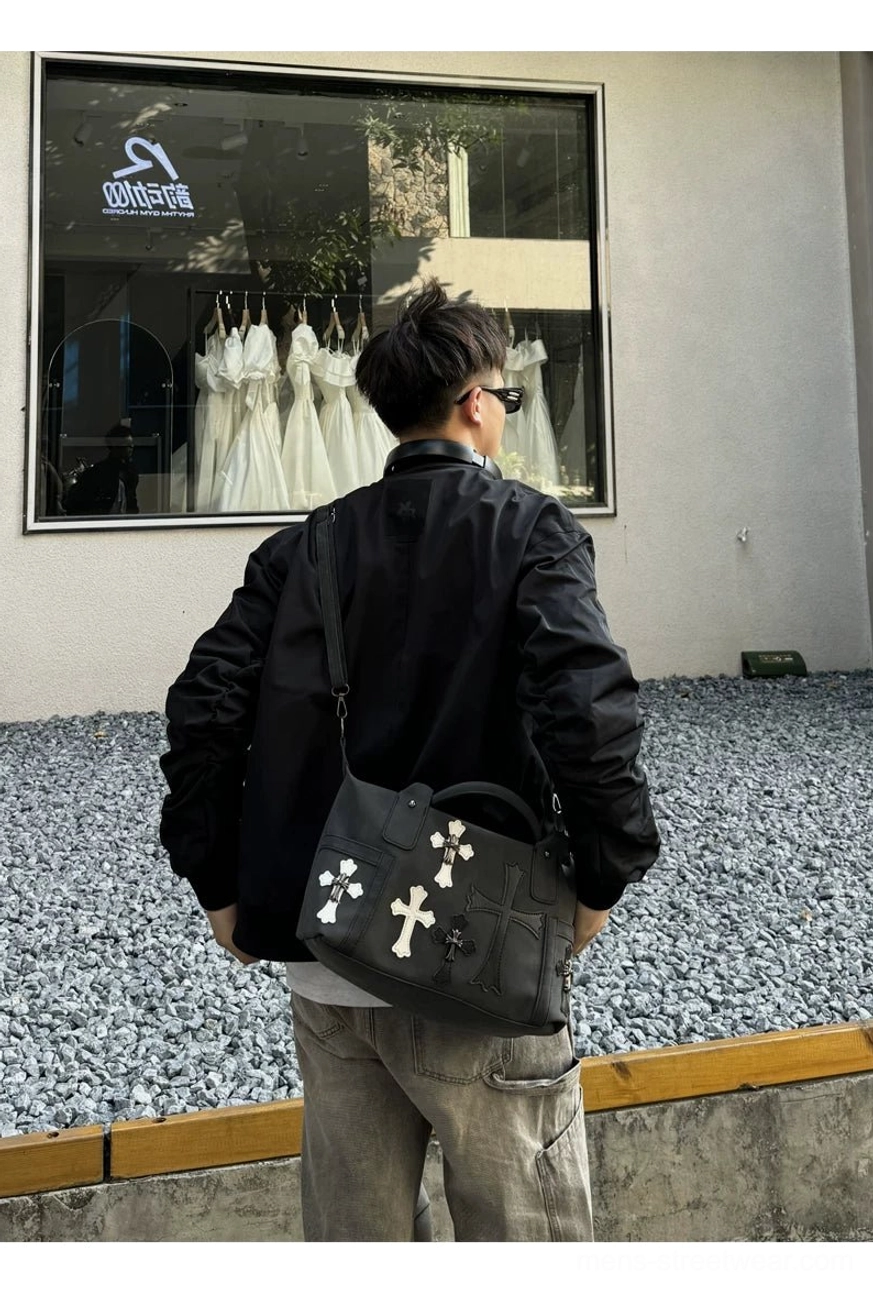 Full rear view of black gothic cross streetwear satchel worn crossbody outdoors showing decorative front panel