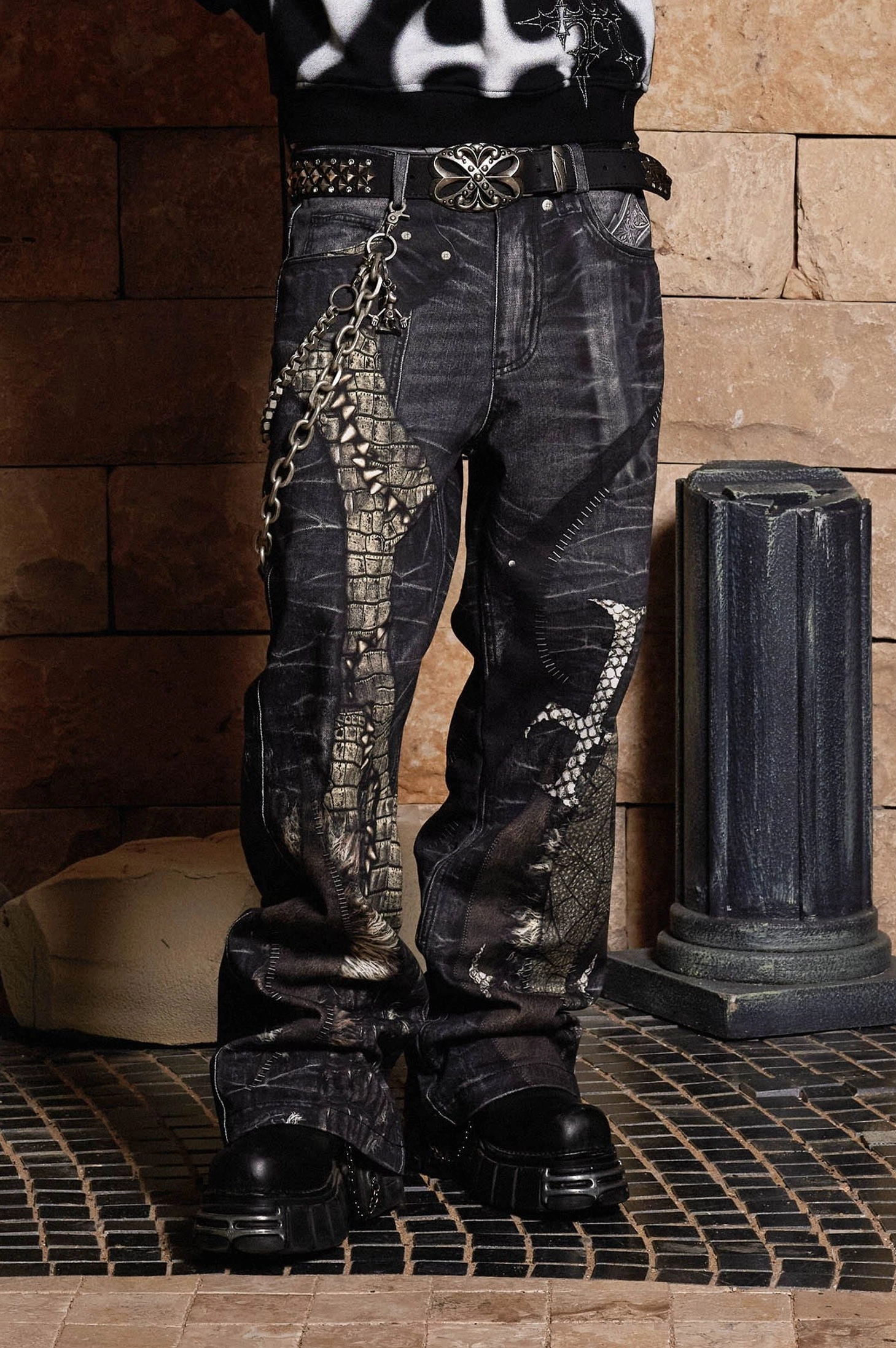 Close-up front view of gothic dragon sword wide-leg jeans showing crocodile-inspired texture, printed graphics, chain belt, and washed charcoal denim